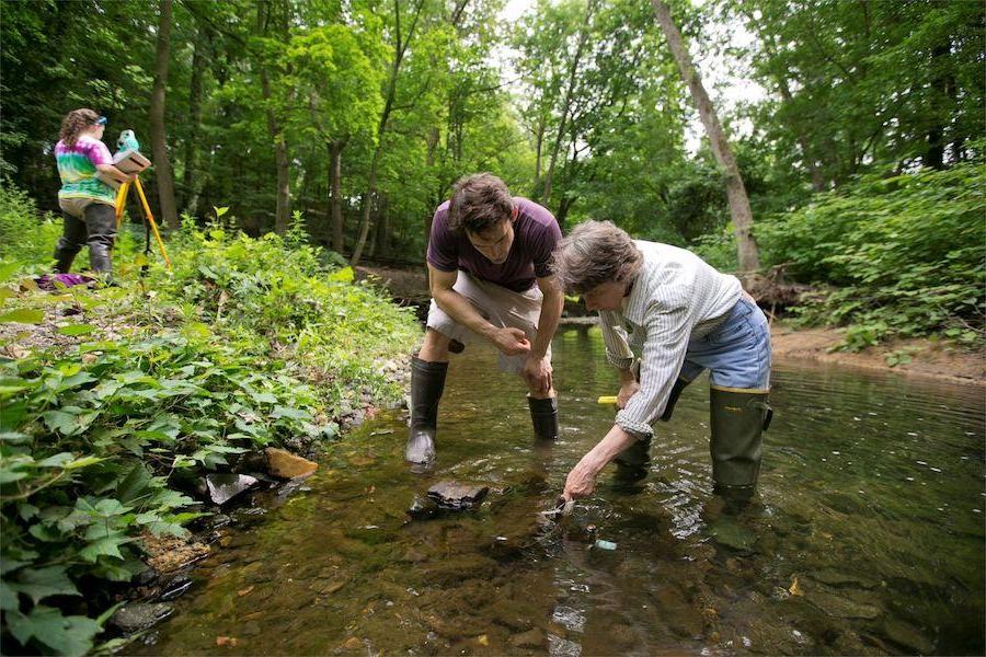 Two environmental science students wearing waders and standing in a stream to test water.